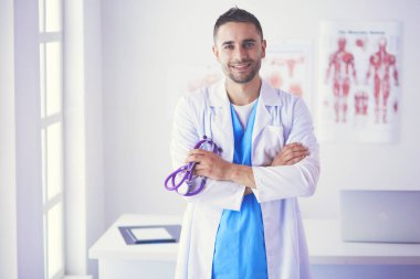 Genç ve kendinden emin erkek doktor portresi tıp ofisinde duruyor..