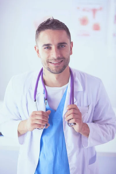 Jonge en zelfverzekerde mannelijke arts portret staan in medisch kantoor. — Stockfoto