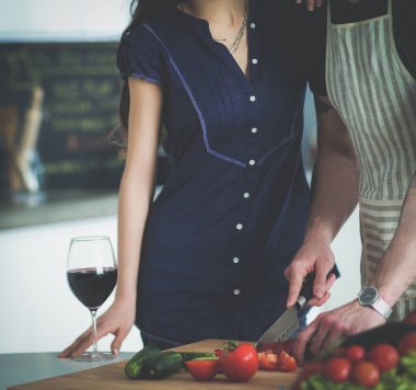 Sebze doğrayan genç bir adam ve mutfakta dizüstü bilgisayarı olan bir kadın.