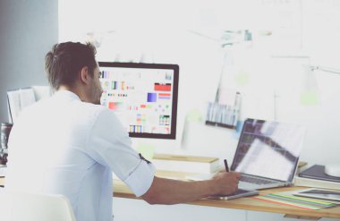 İnternette çalışırken bilgisayarın ve dizüstü bilgisayarın önünde grafik stüdyosunda oturan genç tasarımcının portresi.