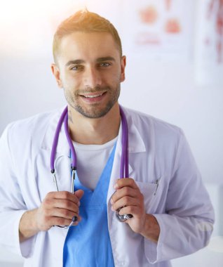 Genç ve kendinden emin erkek doktor portresi tıp ofisinde duruyor..
