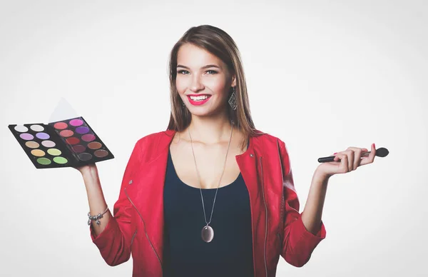 Joven hermosa mujer sostiene en una mano y una paleta con pintura y sombras para el maquillaje, cepillo de segunda mano para maquillaje. — Foto de Stock