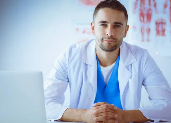 Portrét mužského lékaře s laptopem, který sedí za stolem v lékařské ordinaci — Stock fotografie