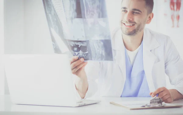 Junger Arzt sitzt an seinem Schreibtisch und analysiert ein Röntgenbild — Stockfoto