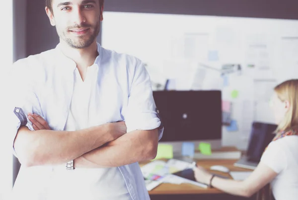 Porträt eines jungen Designers vor Laptop und Computer während der Arbeit. Assistentin bedient ihr Handy im Hintergrund. — Stockfoto