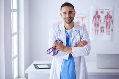 Genç ve kendinden emin erkek doktor portresi tıp ofisinde duruyor..