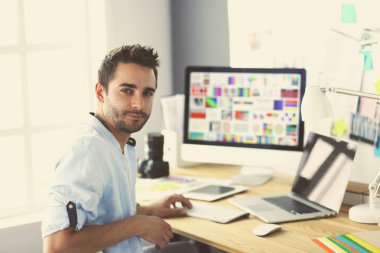 İnternette çalışırken bilgisayarın ve dizüstü bilgisayarın önünde grafik stüdyosunda oturan genç tasarımcının portresi.