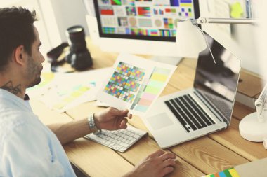 İnternette çalışırken bilgisayarın ve dizüstü bilgisayarın önünde grafik stüdyosunda oturan genç tasarımcının portresi.