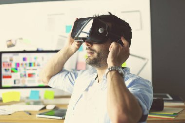 Genç erkek yazılım programcısı ofiste üç boyutlu sanal gerçeklik gözlükleriyle yeni bir uygulama test ediyor..