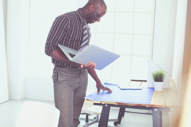 Ofiste bilgisayar ve planlarla çalışan Afrikalı Amerikalı bir mimar.