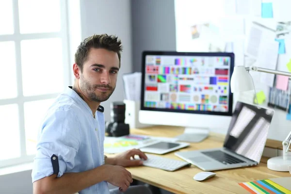 Retrato de jovem designer sentado no estúdio gráfico na frente de laptop e computador enquanto trabalhava online. — Fotografia de Stock