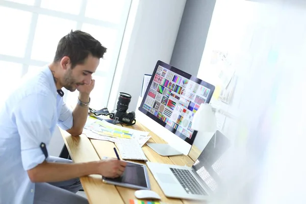 Porträt eines jungen Designers, der im Grafikstudio vor Laptop und Computer sitzt, während er online arbeitet. — Stockfoto