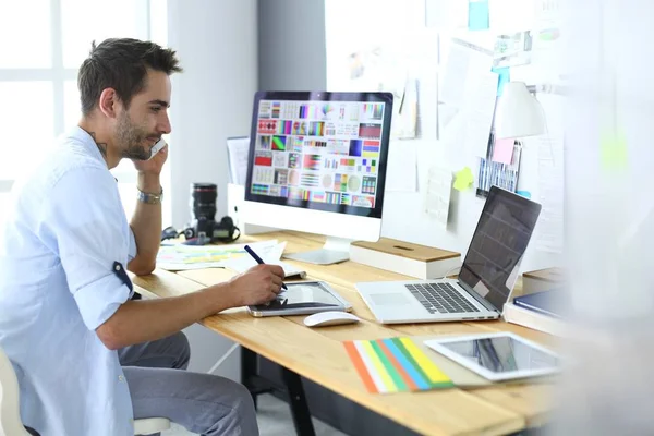 Retrato del joven diseñador sentado en el estudio gráfico frente a la computadora portátil y el ordenador mientras trabaja en línea. — Foto de Stock