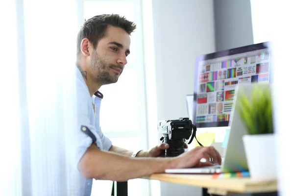 Retrato de jovem designer sentado no estúdio gráfico na frente de laptop e computador enquanto trabalhava online. — Fotografia de Stock