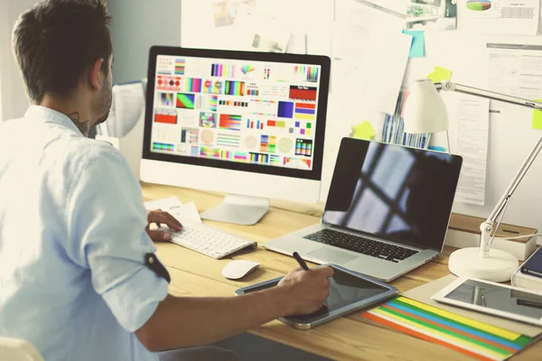 Porträt eines jungen Designers, der im Grafikstudio vor Laptop und Computer sitzt, während er online arbeitet. — Stockfoto