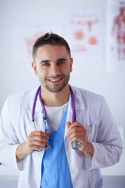 Jonge en zelfverzekerde mannelijke arts portret staan in medisch kantoor. — Stockfoto