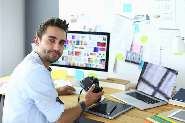 Retrato del joven diseñador sentado en el estudio gráfico frente a la computadora portátil y el ordenador mientras trabaja en línea. — Foto de Stock