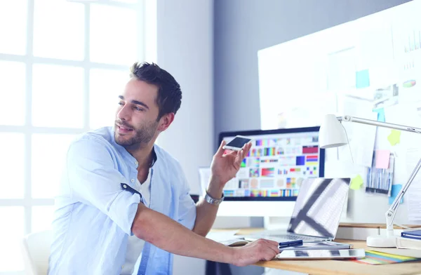 Retrato del joven diseñador sentado en el estudio gráfico frente a la computadora portátil y el ordenador mientras trabaja en línea. — Foto de Stock