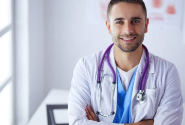 Genç ve kendinden emin erkek doktor portresi tıp ofisinde duruyor.