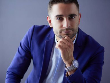 Gri arka planda yalnız oturan genç iş adamı.