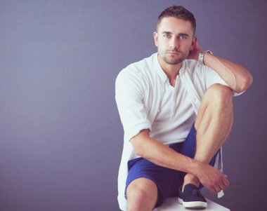 Gri arka planda yalnız oturan genç iş adamı.