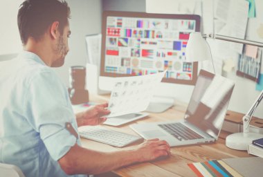 İnternette çalışırken bilgisayarın ve dizüstü bilgisayarın önünde grafik stüdyosunda oturan genç tasarımcının portresi.