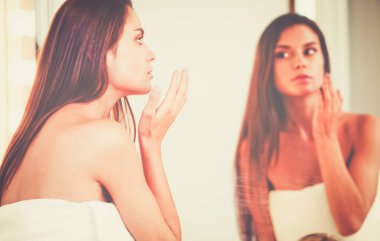 Çekici genç bir kadın yüzüne krem sürüyor.