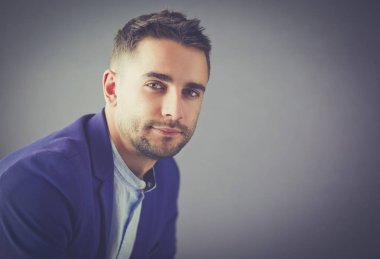 Gri arka planda yalnız oturan genç iş adamı.