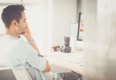 İnternette çalışırken bilgisayarın ve dizüstü bilgisayarın önünde grafik stüdyosunda oturan genç tasarımcının portresi.