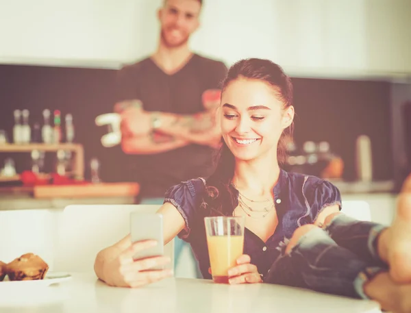 Pareja feliz usando smartphone sentado en la cocina —  Fotos de Stock