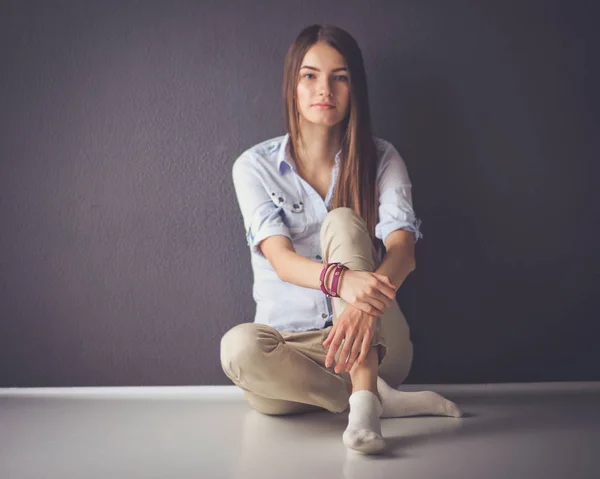Genç bir kadın yerde, kara duvarın yanında oturuyor. — Stok fotoğraf