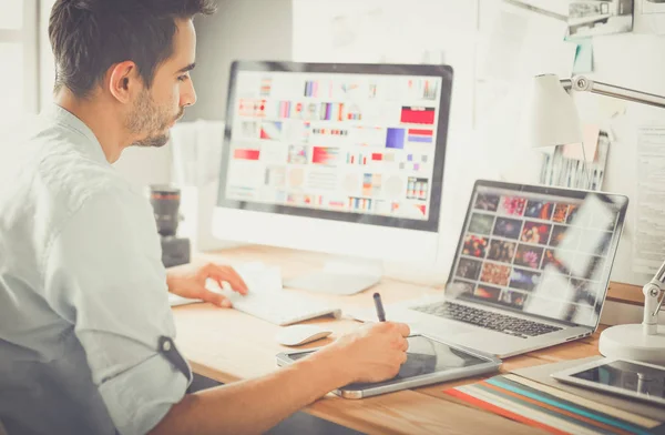 Portrait de jeune designer assis dans un studio graphique devant un ordinateur portable et un ordinateur tout en travaillant en ligne. — Photo