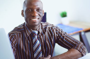 Yakışıklı Afro Amerikalı işadamı Klasik takım elbiseli bir dizüstü bilgisayar kullanarak ve ofiste çalışırken gülümseyen