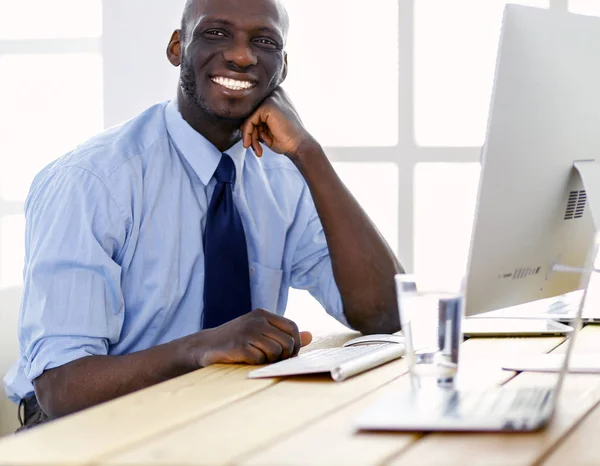Yakışıklı Afro Amerikalı işadamı Klasik takım elbiseli bir dizüstü bilgisayar kullanarak ve ofiste çalışırken gülümseyen — Stok fotoğraf