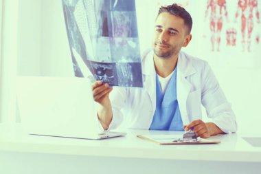 Yakışıklı doktor genç bayan hastasıyla konuşuyor ve ofisinde otururken notlar alıyor..