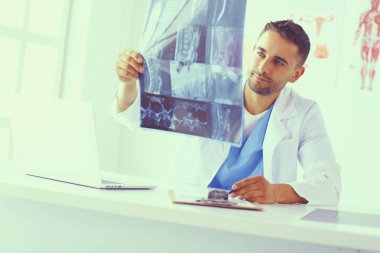 Yakışıklı doktor genç bayan hastasıyla konuşuyor ve ofisinde otururken notlar alıyor..