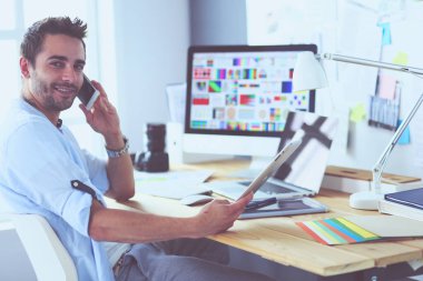 İnternette çalışırken bilgisayarın ve dizüstü bilgisayarın önünde grafik stüdyosunda oturan genç tasarımcının portresi.