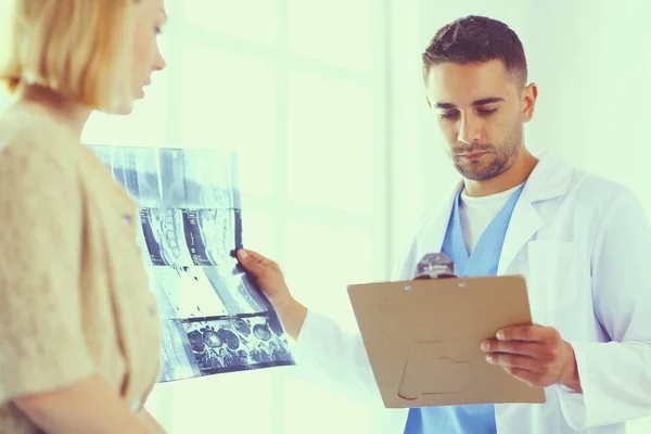 El guapo doctor está hablando con una paciente joven y tomando notas mientras está sentado en su consultorio.. —  Fotos de Stock