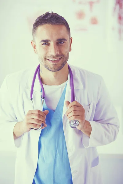 Jonge en zelfverzekerde mannelijke arts portret staan in medisch kantoor. — Stockfoto