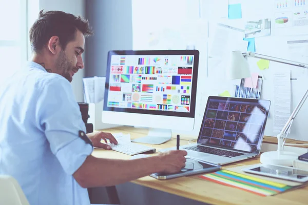 Porträt eines jungen Designers, der im Grafikstudio vor Laptop und Computer sitzt, während er online arbeitet. — Stockfoto