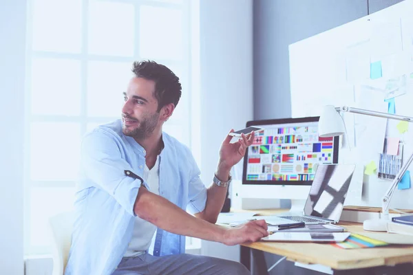 Retrato del joven diseñador sentado en el estudio gráfico frente a la computadora portátil y el ordenador mientras trabaja en línea. — Foto de Stock