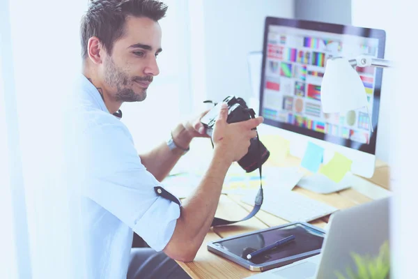 Retrato del joven diseñador sentado en el estudio gráfico frente a la computadora portátil y el ordenador mientras trabaja en línea. — Foto de Stock