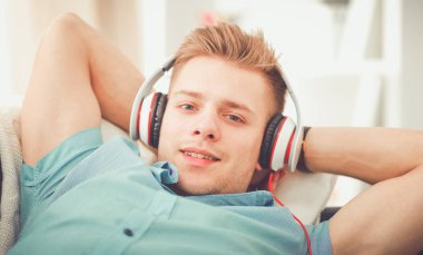 Kanepede müzik dinleyen genç yakışıklı bir adam.