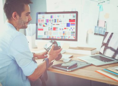 İnternette çalışırken bilgisayarın ve dizüstü bilgisayarın önünde grafik stüdyosunda oturan genç tasarımcının portresi.