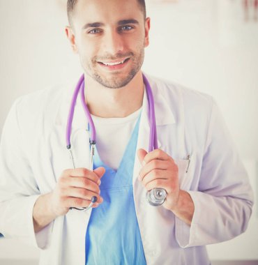 Genç ve kendinden emin erkek doktor portresi tıp ofisinde duruyor..