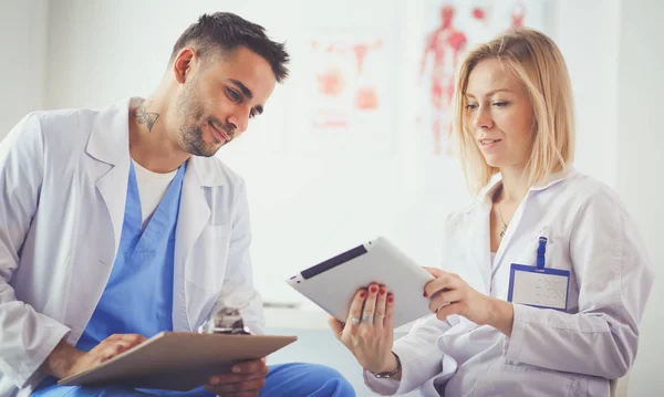 Snygg läkare pratar med ung kvinnlig läkare och antecknar när han sitter på sitt kontor. — Stockfoto