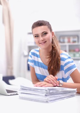 Elinde belgelerle masanın üstünde oturan gülümseyen kadın..