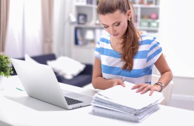 Elinde belgelerle masanın üstünde oturan gülümseyen kadın..