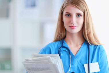 Hastane koridorunda steteskoplu kadın doktor portresi, elinde klasör var..
