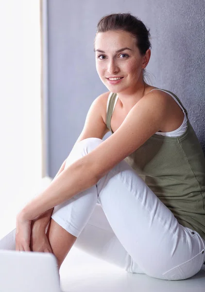 Attraktive kaukasische Mädchen sitzt auf dem Boden mit Tasse und Tablette in der Nähe der Wand — Stockfoto